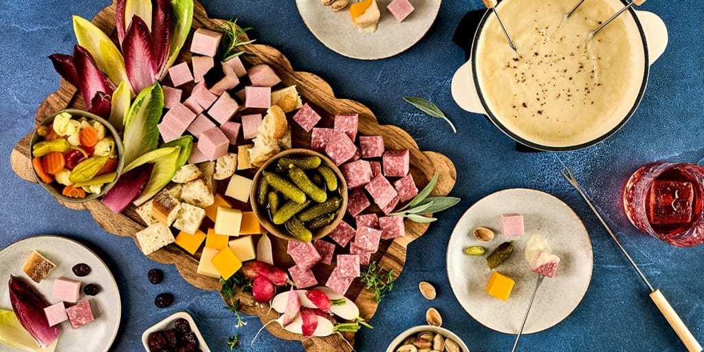 A table spread featuring a platter of cubed deli meats, cheeses, and dipping sauces.