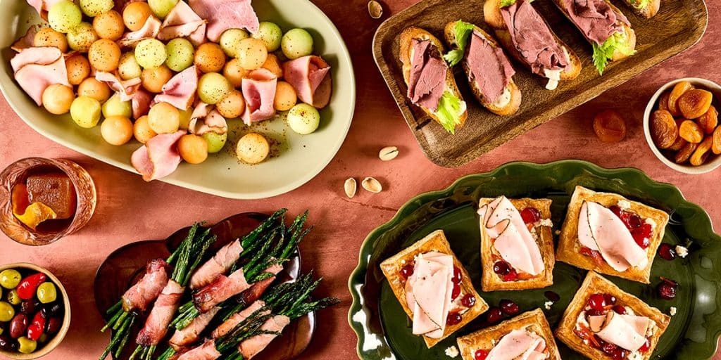 A grid collage featuring four festive holiday appetizer dishes, including roasted potatoes, pinwheels, rolled meats, and sliced bread appetizers.