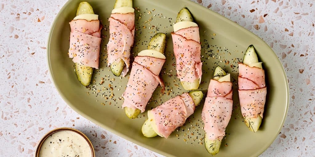 A platter of dill pickle spears wrapped in sliced deli meat and cheese.