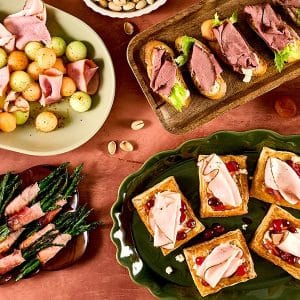 A grid collage featuring four festive holiday appetizer dishes, including roasted potatoes, pinwheels, rolled meats, and sliced bread appetizers.